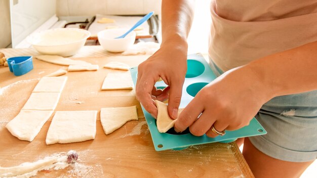 Imagen de primer plano de una mujer joven recogiendo un trozo de masa y poniéndola en forma de silicona para hornear en el horno