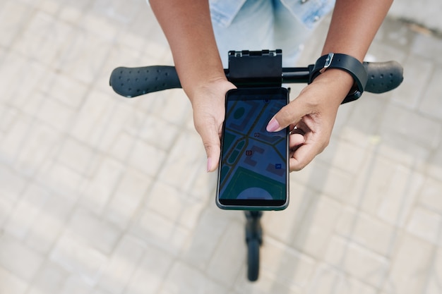 Imagen de primer plano de una mujer joven siguiendo el mapa a través de la aplicación de teléfono inteligente cuando viaja en scooter