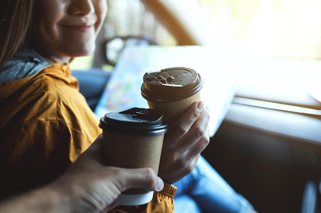 Imagen de primer plano de una mujer joven sosteniendo un mapa y tintineando una taza de café con un amigo mientras viajaba en el auto