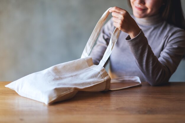 Imagen de primer plano de una mujer joven sosteniendo y mirando dentro de una bolsa de tela blanca para un concepto reutilizable y ambiental