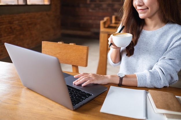 Imagen de primer plano de una mujer joven tomando café y trabajando en una computadora portátil