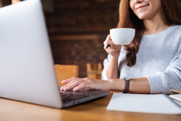 Imagen de primer plano de una mujer joven tomando café y trabajando en una computadora portátil