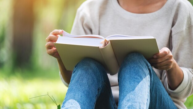 Imagen de primer plano de una mujer leyendo un libro mientras está sentada en el parque