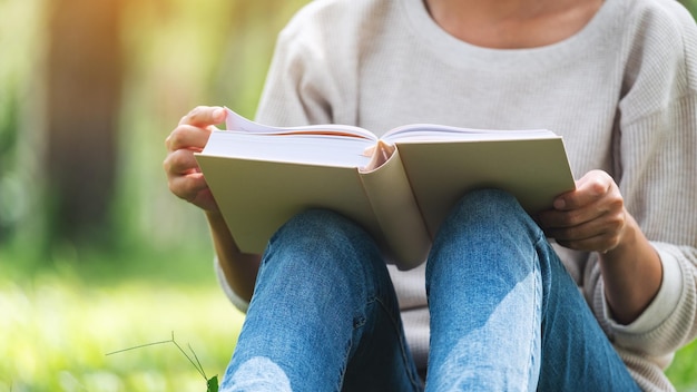 Foto imagen de primer plano de una mujer leyendo un libro mientras está sentada en el parque