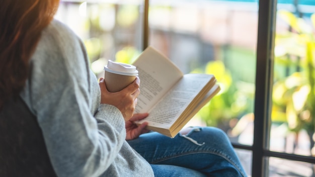 Imagen de primer plano de una mujer leyendo un libro y tomando café por la mañana