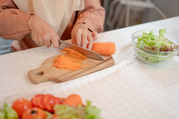 Imagen en primer plano de una mujer musulmana cortando zanahorias con un cuchillo en una tabla de cortar