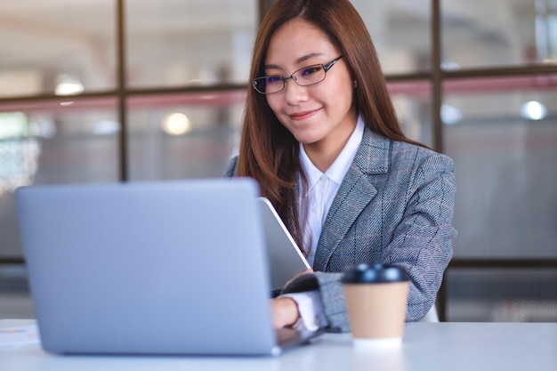 Imagen de primer plano de una mujer de negocios asiática que usa una tableta digital y una computadora portátil en la oficina