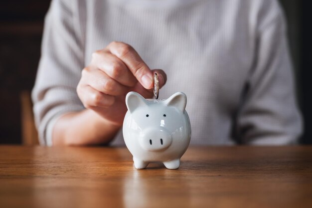 Imagen de primer plano de una mujer poniendo monedas en una alcancía para ahorrar dinero concepto