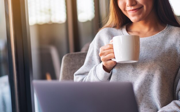 Imagen de primer plano de una mujer que trabaja en una computadora portátil mientras bebe café en la cafetería