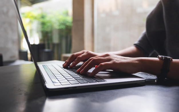 Imagen de primer plano de una mujer que trabaja y escribe en el teclado de la computadora portátil en la mesa de madera