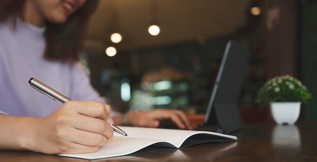 Imagen de primer plano de una mujer que usa un bolígrafo para escribir en un cuaderno o en un informe en papel en la oficina