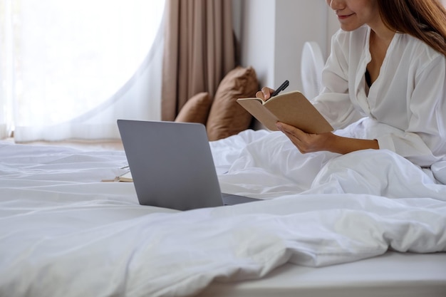 Imagen de primer plano de una mujer que usa y trabaja en una computadora portátil mientras está sentada en la cama en casa