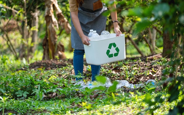 Foto imagen de primer plano de una mujer recogiendo y poniendo botellas de plástico en una papelera de reciclaje al aire libre