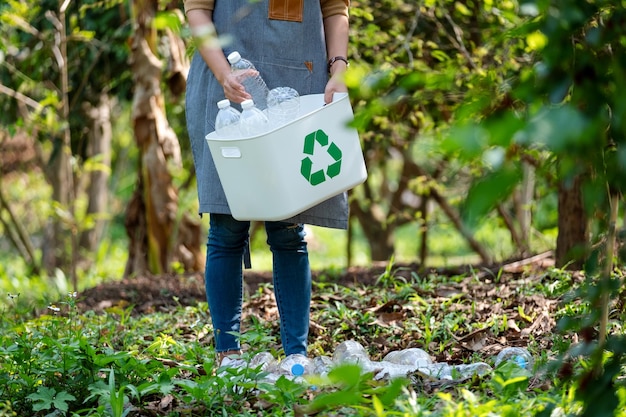 Imagen de primer plano de una mujer recogiendo y poniendo botellas de plástico en una papelera de reciclaje al aire libre