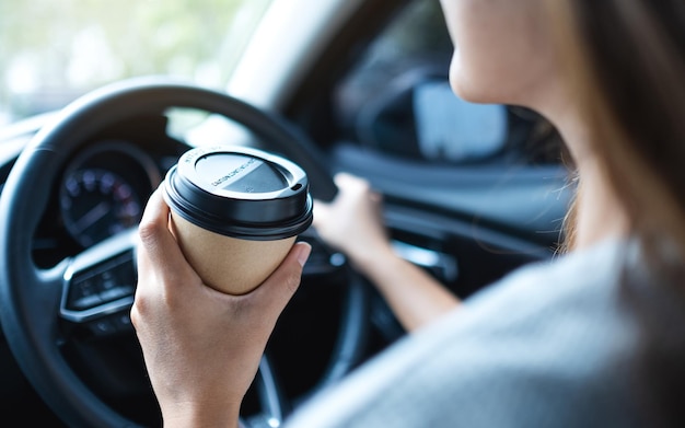 Imagen de primer plano de una mujer sosteniendo y bebiendo café mientras conduce un automóvil