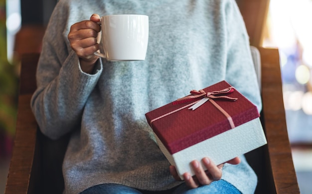 Imagen de primer plano de una mujer sosteniendo una caja de regalo mientras bebe café