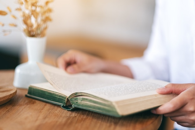 Imagen de primer plano de una mujer sosteniendo y leyendo un libro de novela vintage sobre mesa de madera