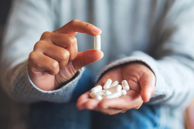 Imagen de primer plano de una mujer sosteniendo y mostrando cápsulas de medicina blanca en la mano