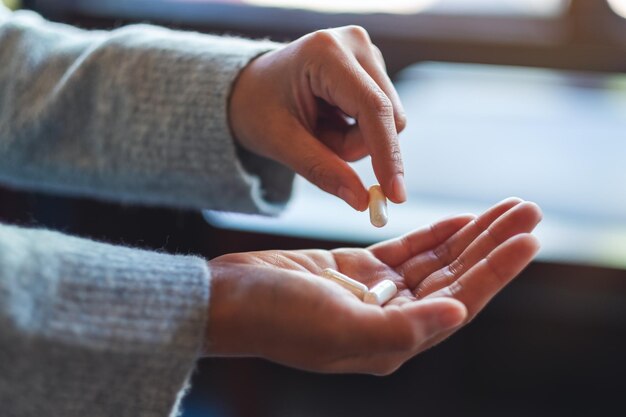 Imagen de primer plano de una mujer sosteniendo y recogiendo cápsulas de medicina blanca en la mano