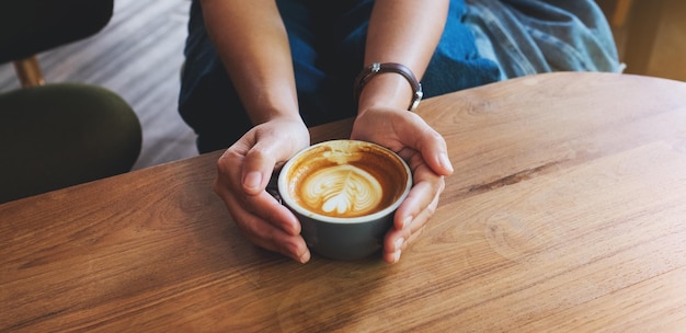 Imagen de primer plano de una mujer sosteniendo una taza de café con arte latte