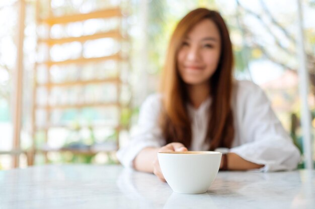 Imagen de primer plano de una mujer sosteniendo una taza de café caliente sobre la mesa