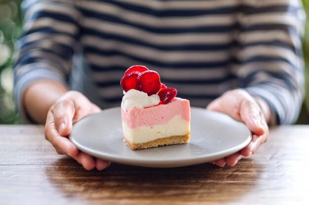 Imagen de primer plano de una mujer sosteniendo un trozo de tarta de queso con fresas