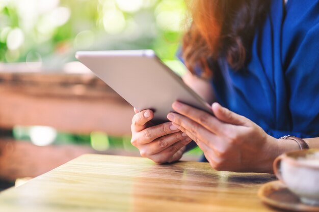 Imagen de primer plano de una mujer sosteniendo y usando tablet pc mientras está sentado en el jardín