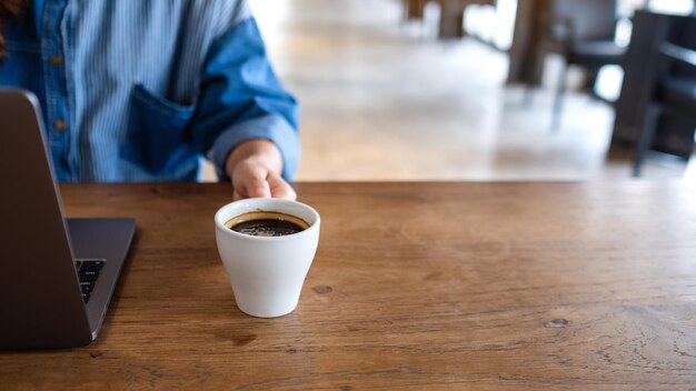 Imagen de primer plano de una mujer tomando café mientras usa y trabaja en una computadora portátil