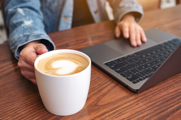 Foto imagen de primer plano de una mujer usando y tocando en el panel táctil de la computadora portátil en la mesa de madera mientras bebe café