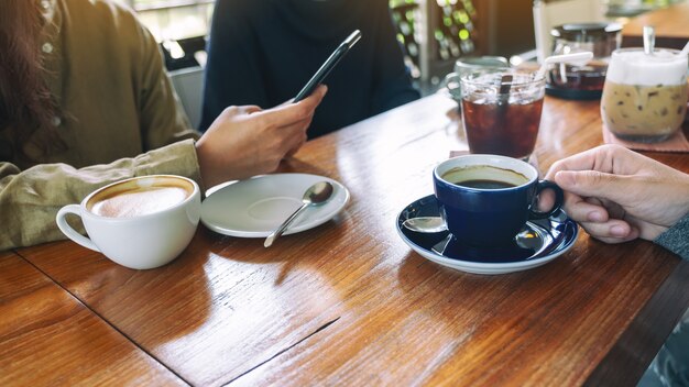 Imagen de primer plano de personas que usan teléfonos móviles y beben café juntos en la cafetería