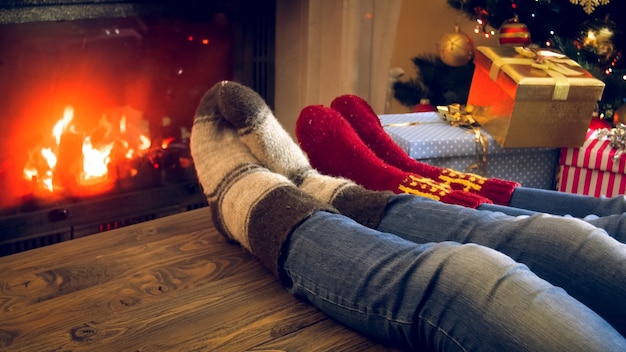 Imagen de primer plano de los pies de la familia en calcetines de lana acostado sobre la mesa de madera junto a la chimenea encendida