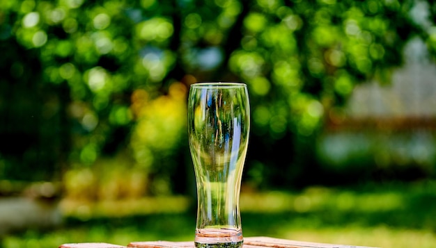 Imagen de primer plano de un vaso de cerveza ampty sobre una mesa de madera marrón El sol brilla a través del vidrio Fondo de naturaleza verde borroso