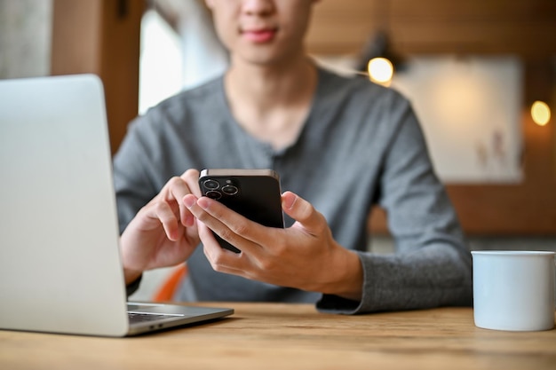 Imagen recortada de un apuesto joven asiático usando su teléfono en una mesa en la cafetería