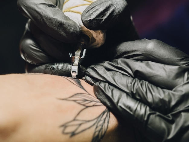 Imagen recortada de una artista haciendo un tatuaje en la mano de un cliente masculino