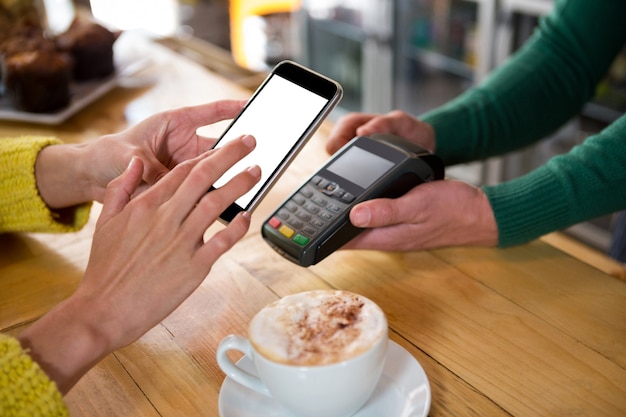 Imagen recortada del barista aceptando el pago a través de un teléfono inteligente en el café