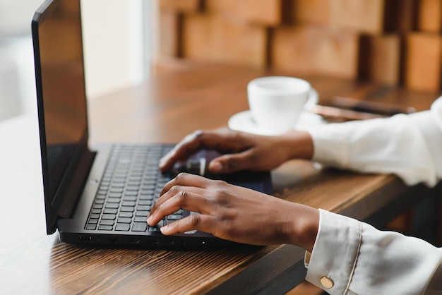 Imagen recortada de una chica afroamericana tomando café mientras trabaja con una laptop en un café