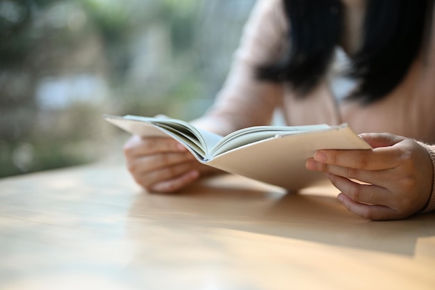 Imagen recortada de una chica asiática leyendo un libro en una mesa en la cafetería