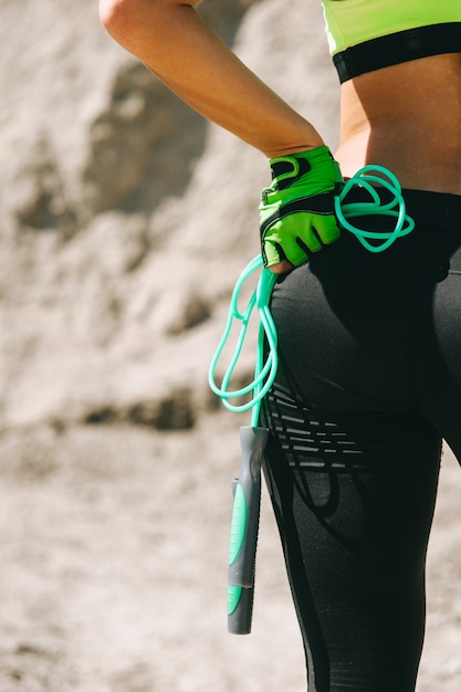 Imagen recortada de la chica de deportes en pantalones de sudor y zapatillas que saltar la cuerda en el sol de la mañana