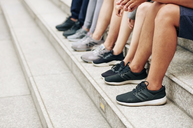 Imagen recortada de deportistas en pantalones cortos y zapatillas de deporte sentados en los pasos después del entrenamiento al aire libre