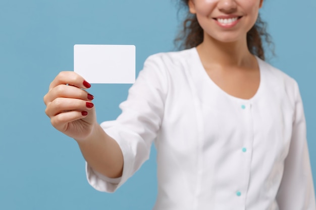 Imagen recortada de una doctora afroamericana aislada de fondo azul. El médico con bata médica blanca tiene una tarjeta bancaria de crédito vacía en blanco. Concepto de medicina del personal sanitario. Simulacros de espacio de copia.