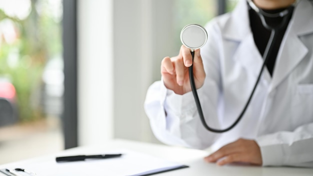 Imagen recortada de una doctora asiática en uniforme sosteniendo un estetoscopio en su escritorio