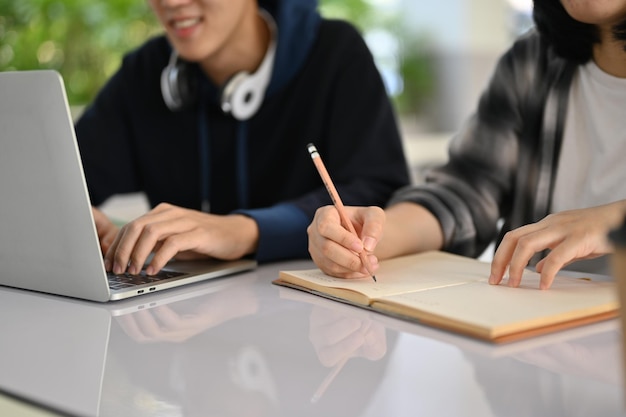 Imagen recortada de dos jóvenes estudiantes universitarios asiáticos haciendo juntos su proyecto escolar