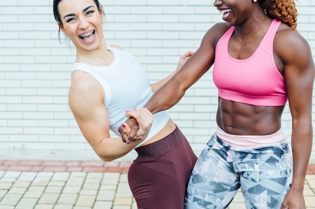 Imagen recortada de dos mujeres cogidos de la mano. La mano de la izquierda es de una joven blanca. El de la derecha es de una joven negra.