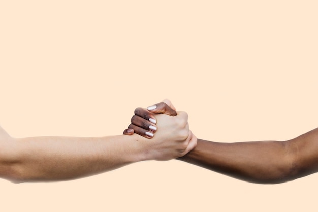 Imagen recortada de dos mujeres cogidos de la mano. La mano de la izquierda es de una joven blanca con uñas grises. El de la derecha es de una joven negra.