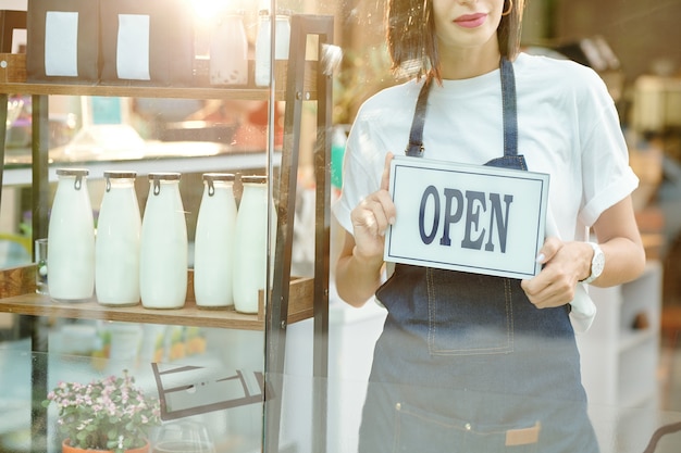 Imagen recortada de la dueña de una tienda sosteniendo un cartel abierto y dando la bienvenida a los clientes dentro