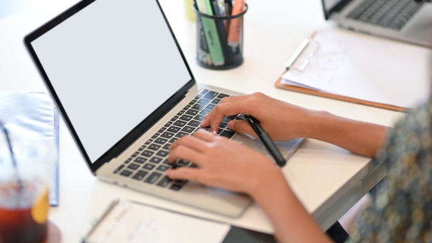 Imagen recortada de empresaria escribiendo en el teclado de la computadora portátil con maqueta de pantalla en blanco