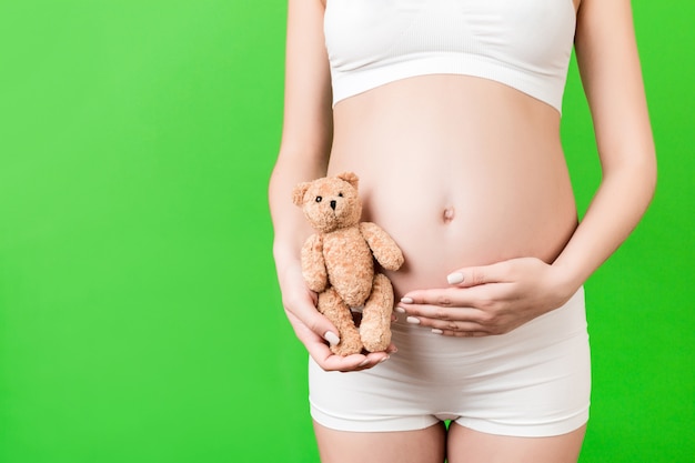 Imagen recortada de feliz mujer embarazada en ropa interior blanca con oso de peluche contra su vientre