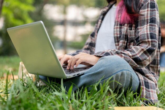 Una imagen recortada de una hembra usando su computadora portátil mientras está sentada en la hierba en un parque