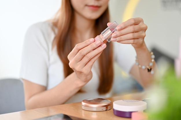 Imagen recortada Hermosa mujer asiática joven sosteniendo un lápiz labial haciendo su maquillaje diario