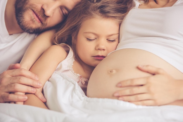 Imagen recortada de una hermosa mujer embarazada, su apuesto esposo y su linda hijita durmiendo juntos en la cama